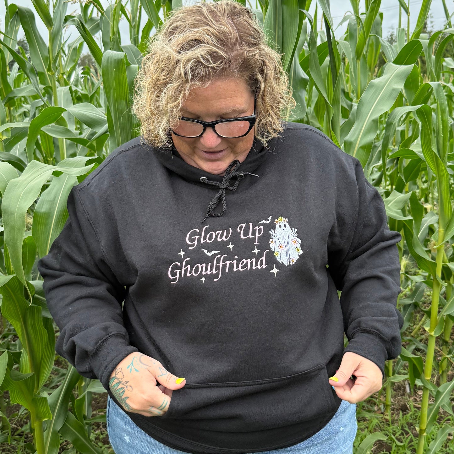 Person wearing a black hoodie with text standing in a field of tall green plants.