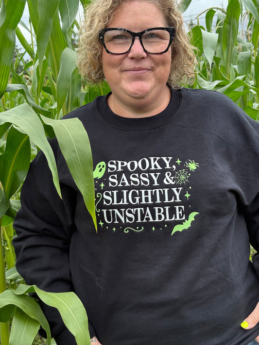 Person wearing a black sweatshirt with text and graphics, standing among green leaves.
