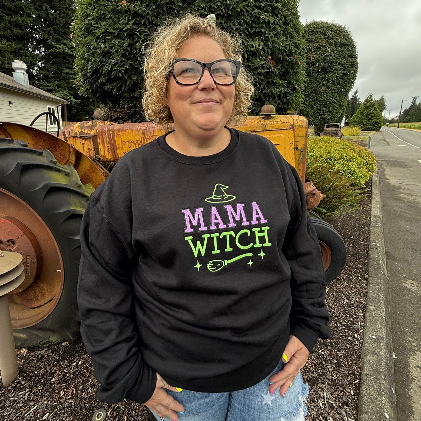 Person wearing a 'Mama Witch' hoodie standing next to a wooden barrel outdoors.