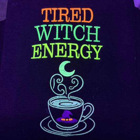 Black shirt with 'Tired Witch Energy' text and witch graphic under black light